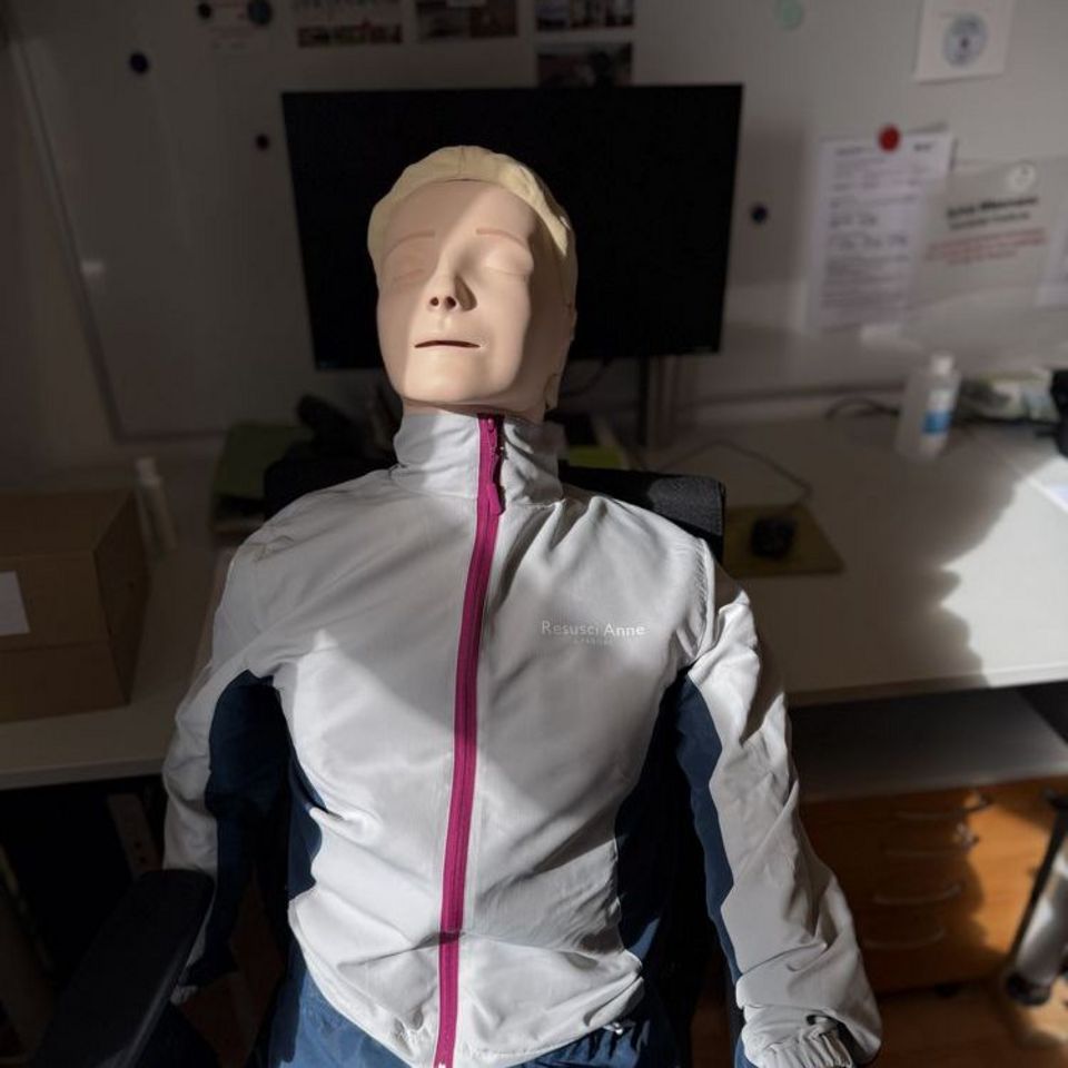 Reanimationspuppe im Sonnenlicht sitzend auf Bürostuhl (Puppe hat auch Arme und Beine)