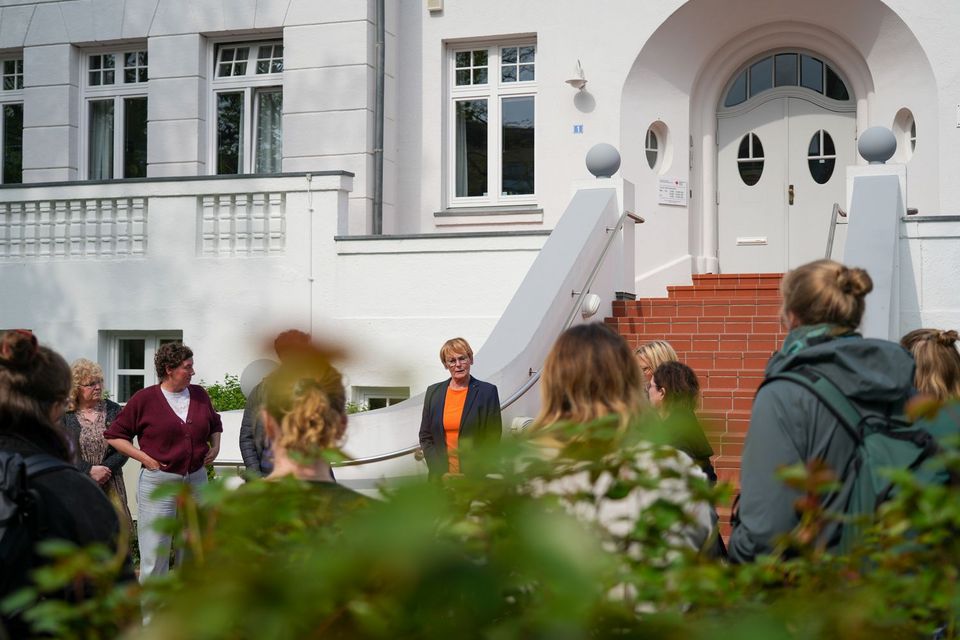 Eine Gruppe Menschen steht in einem Kreis vor einem großen weißen Gebäude.